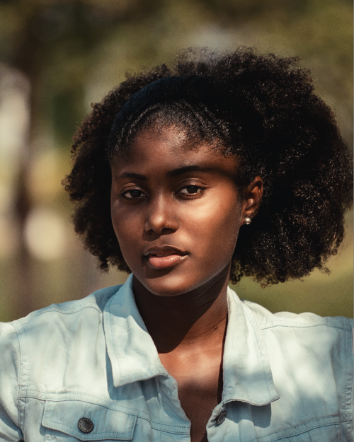 Free Close-up portrait of a young woman in denim jacket with natural hair outdoors. Stock Photo