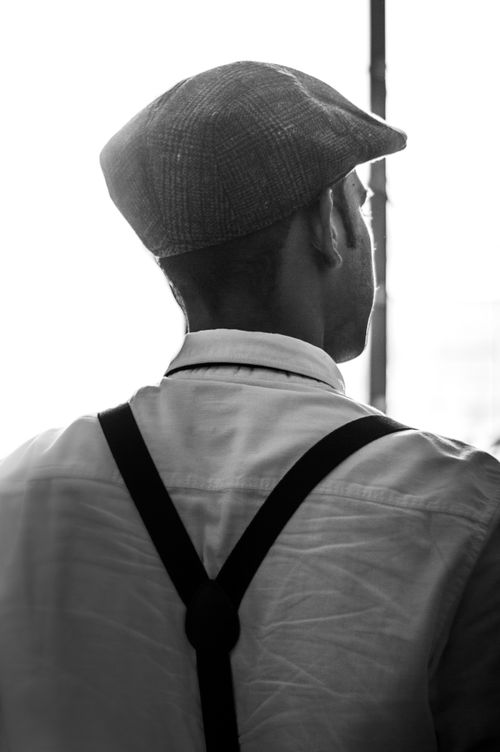 Free Black and white image of a man wearing a flat cap and suspenders, captured from behind. Stock Photo
