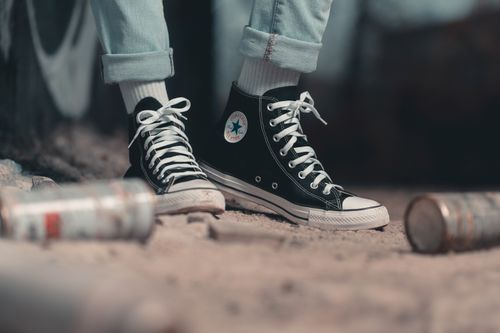 Free Close-up of stylish black retro sneakers amidst spray cans on a gritty urban street. Stock Photo