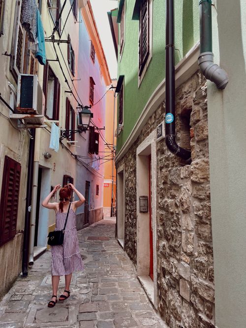 Free Woman walking in a colorful, historic alley in Piran, Slovenia. Captures old-world charm. Stock Photo