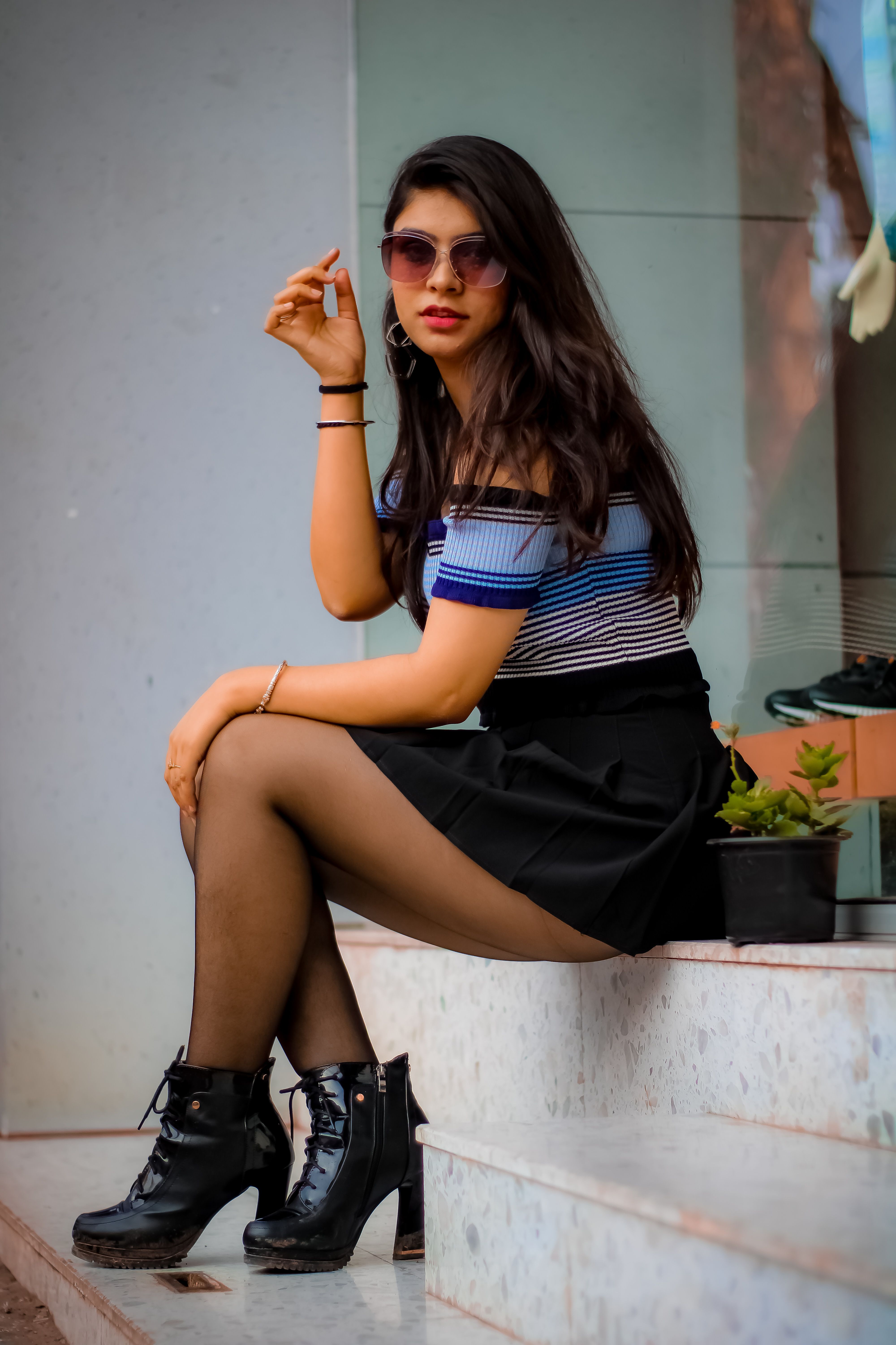 Stylish woman in a black skirt and sunglasses sitting on stairs, exuding confidence.