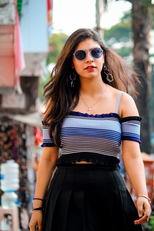 Free Stylish woman in off-shoulder striped top and sunglasses walking confidently on a vibrant street. Stock Photo