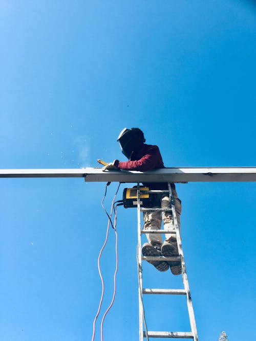 Low Angle Shot of a Man Standing on a Ladder and Welding 