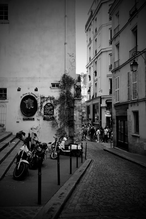 Grayscale Photo of Buildings With Motorcycle Beside