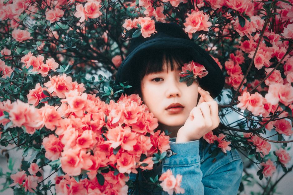 Portrait of an Asian woman surrounded by vibrant pink blossoms, creating a dreamy outdoor scene.