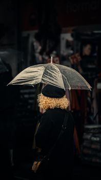 Woman with curly hair and umbrella in rainy Istanbul street, capturing a moody atmosphere.