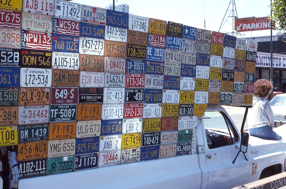 Photo by Malcolm Hill A vibrant arrangement of license plates mounted on a white truck parked outdoors.