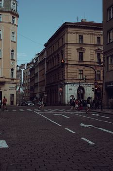 A bustling city intersection with pedestrians and historic buildings on a cloudy day.