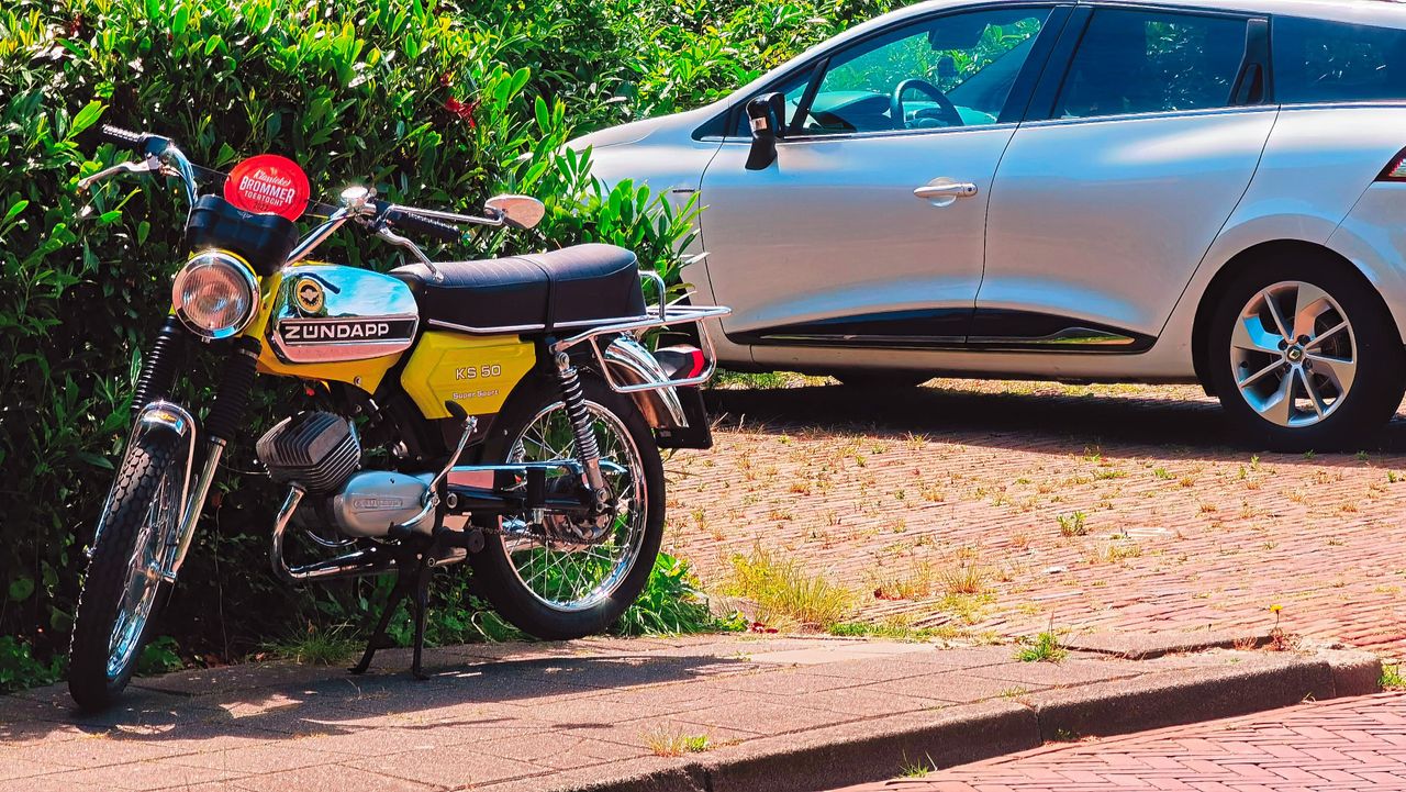 a classic zundapp ks50 motorcycle parked beside a modern car on a sunl