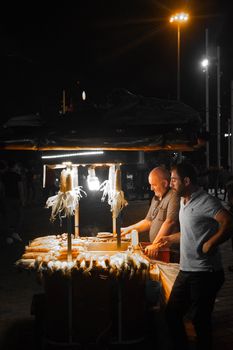 Two men selling corn at a night market, illuminated by warm lights.