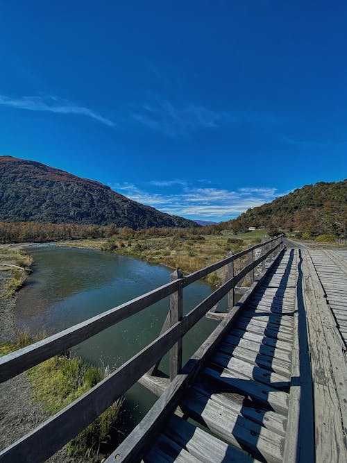 A Wooden Bridge Near the River and Mountains with Green Trees