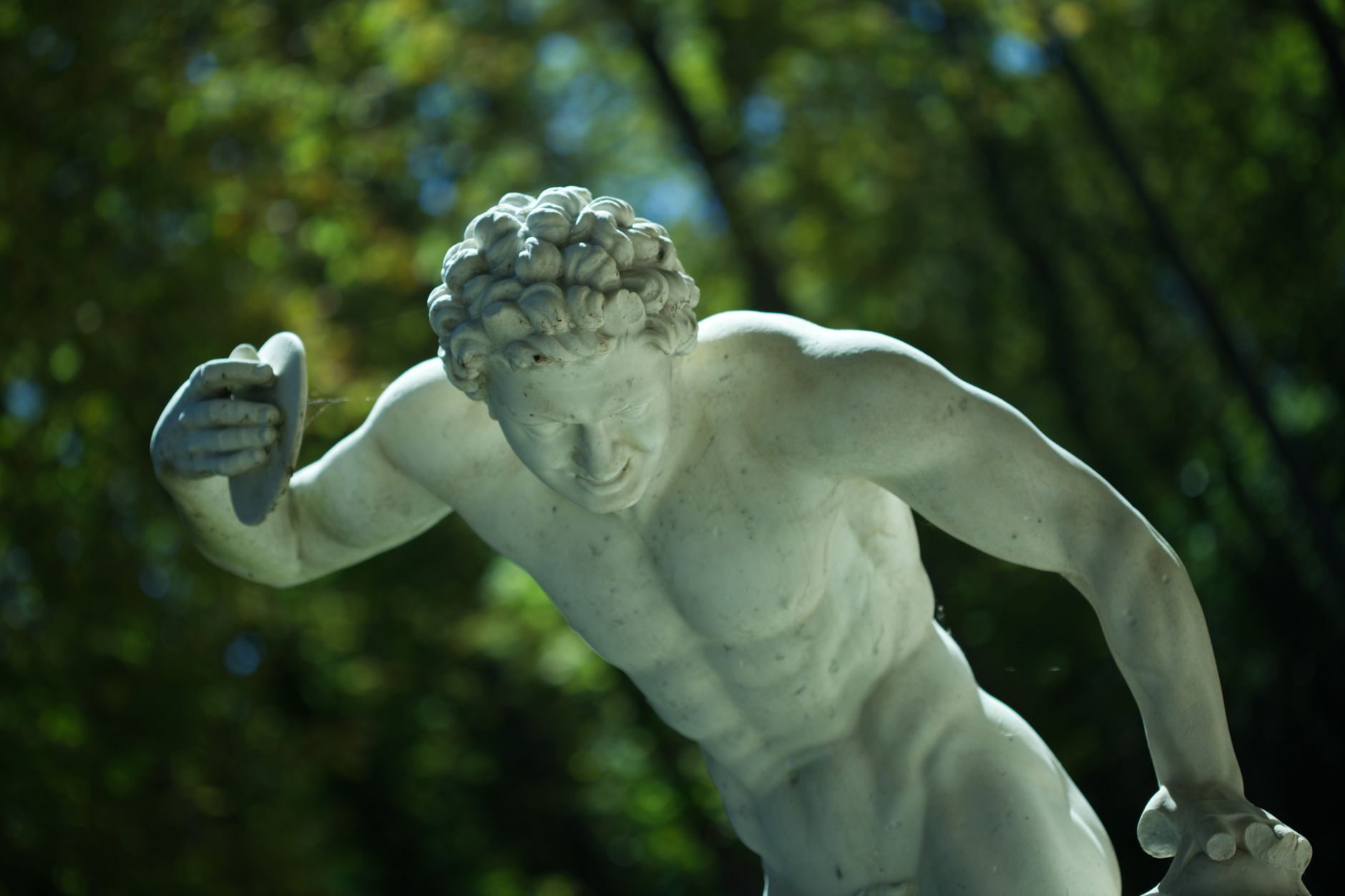 Close-up of a classical marble statue depicting a discus thrower with a vibrant outdoor background.
