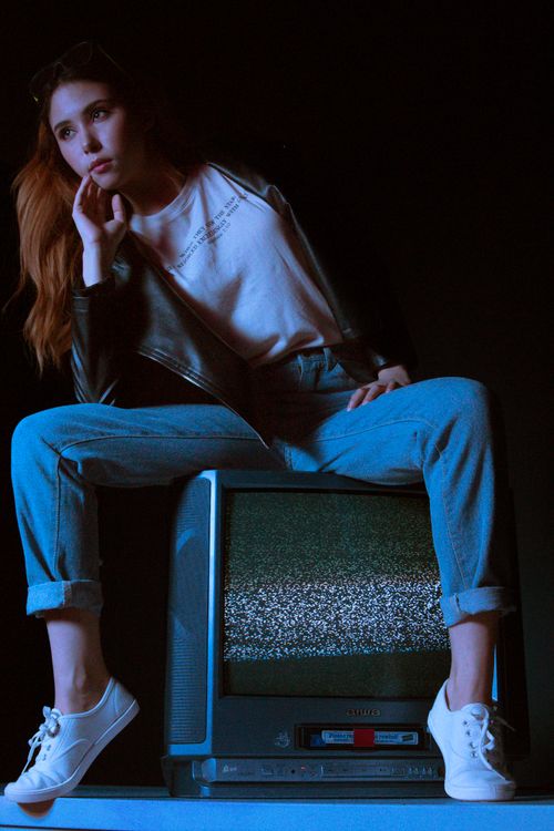 Free Fashionable woman in jeans and jacket poses on old TV with static in a moody studio setting. Stock Photo