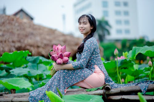 女人拿着粉红色的花瓣花，坐在棕色木制面板上