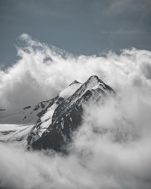 Free Dramatic view of snow-covered mountain peaks surrounded by clouds, perfect for scenic nature themes. Stock Photo