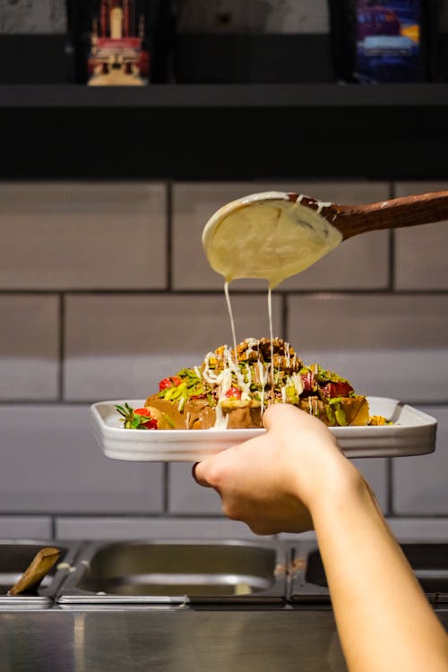 Person Pouring Sauce on Meal in Kitchen