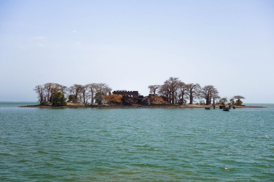 Remote island with historic ruins and trees in Gambia, serene ocean backdrop.