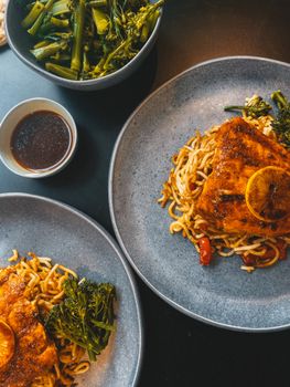 Tasty grilled salmon with lemon, served with noodles and fresh broccolini.