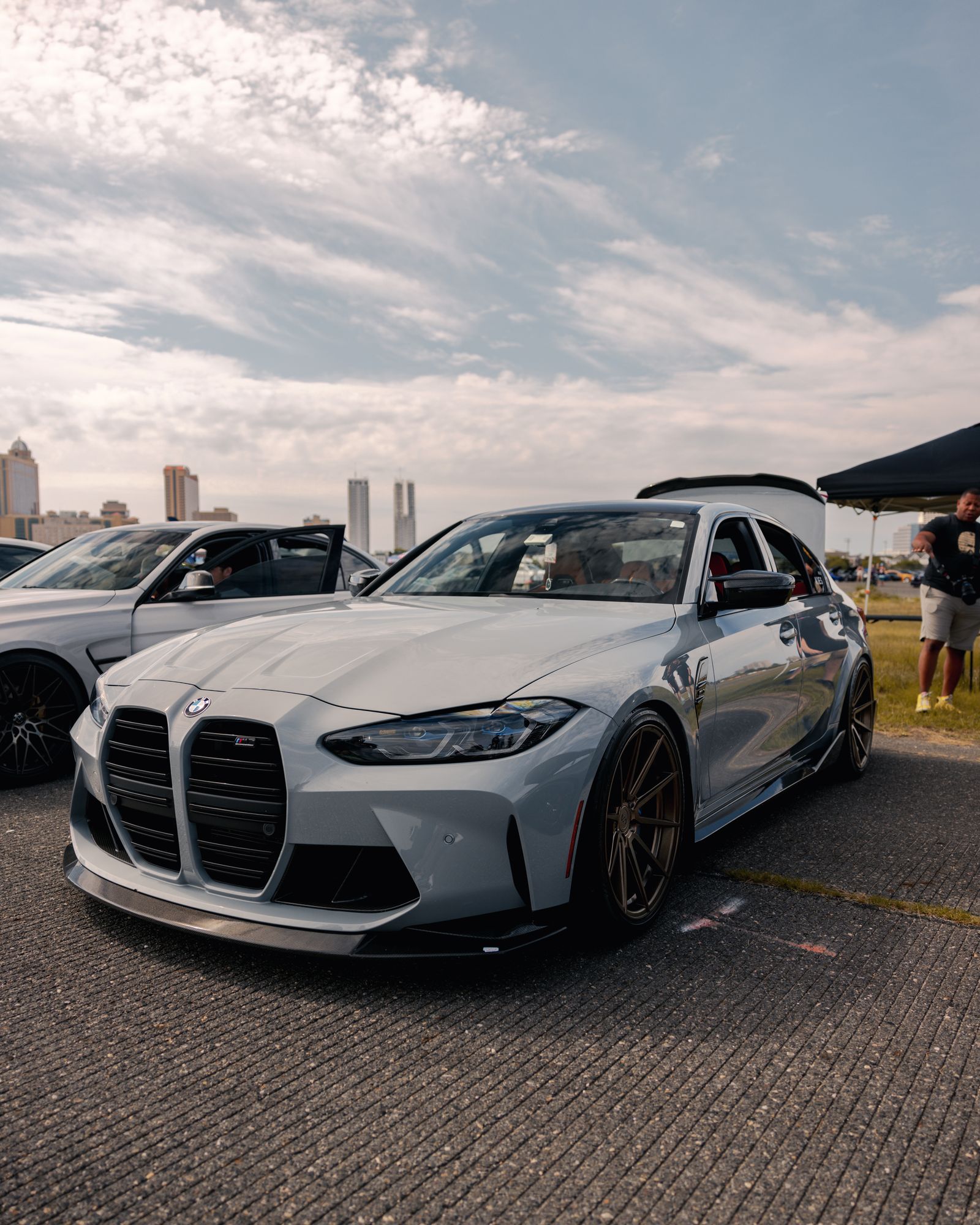 Gray BMW G80 M3 front three-quarter view parked at a car meet on aftermarket bronze wheels