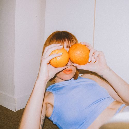 Free A woman playfully covers her eyes with oranges in a quirky indoor portrait. Stock Photo