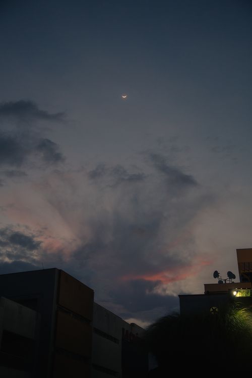 Free Dramatic dusk skyline featuring silhouette of buildings under a crescent moon and colorful clouds. Stock Photo