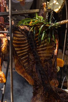 Delicious grilled meat with fresh herbs hanging over flames in an outdoor barbecue setting.
