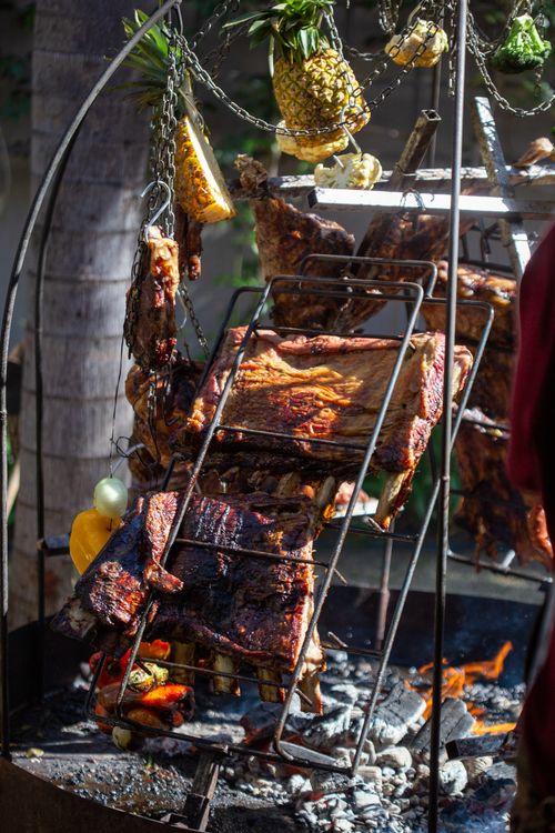 Free Charcoal grilling with meats and pineapples outdoors, showcasing rustic cooking methods over open flame. Stock Photo