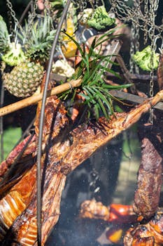 Succulent meats and fruits grilling over an open flame at an outdoor barbecue.