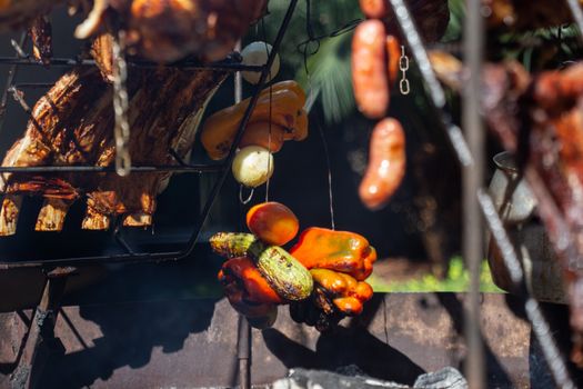 Vibrant assortment of grilled vegetables and meats on an outdoor barbecue grill in daylight.