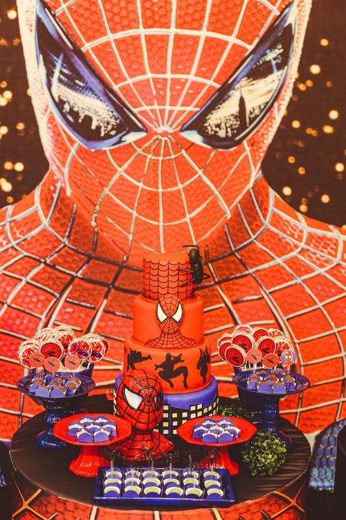 Superhero-themed birthday cake with Spider-Man decorations and snacks arranged on a colorful party table
