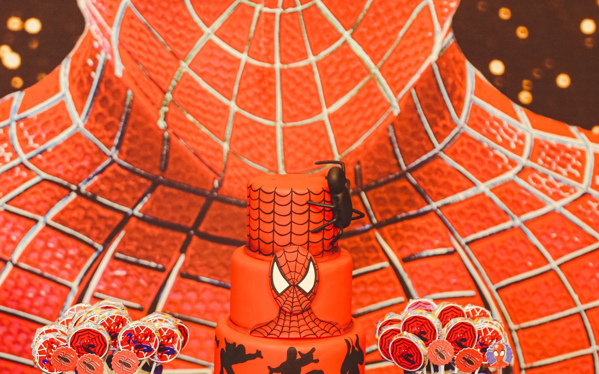 Superhero-themed birthday cake with Spider-Man decorations and snacks arranged on a colorful party table