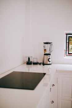 Stylish kitchen corner featuring a sleek blender and induction stove on a white countertop.