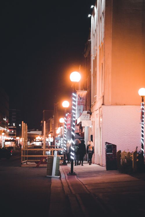 Free A vibrant urban night scene showcasing a well-lit street with people walking under glowing streetlights. Stock Photo