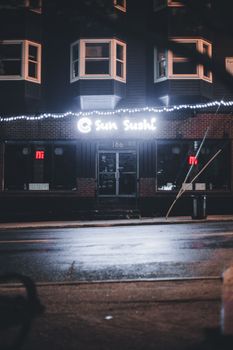 A neon-lit sushi restaurant on a quiet city street at night, capturing urban ambiance.