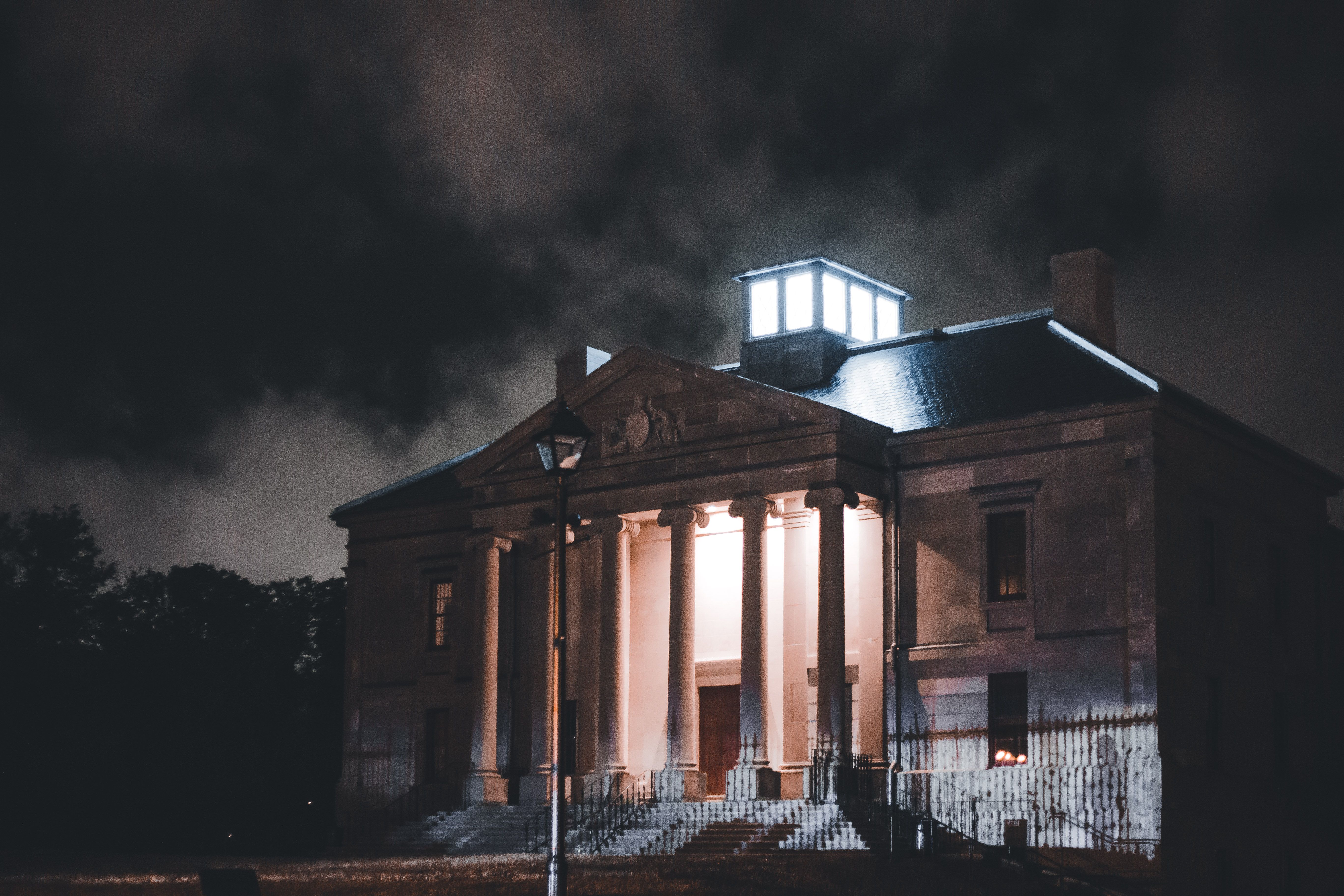 An atmospheric night view of a historic building with illuminated columns against a dramatic sky.