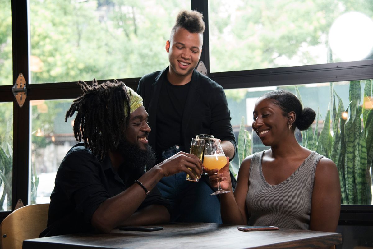 Three friends toasting with clear glasses filled with beverages near a window