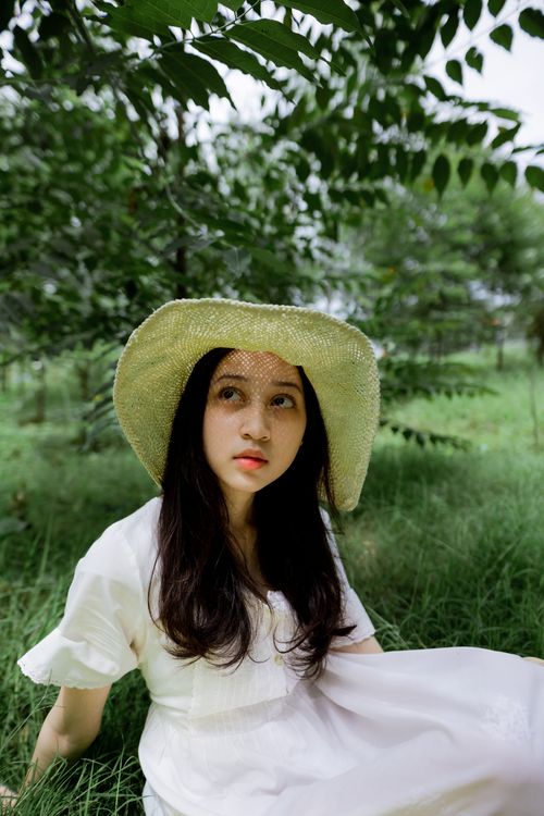 Free Asian woman in straw hat sitting on grass in a summer garden. Stock Photo