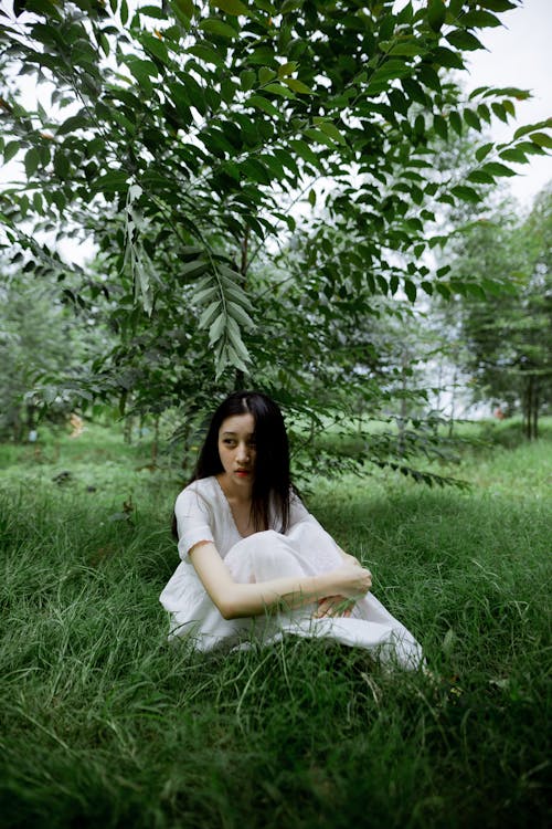 Woman in White Dress Sitting on the Grassy Field