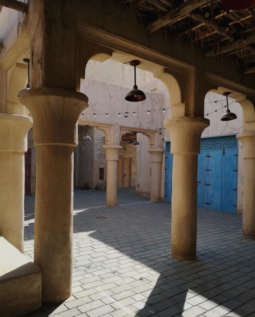 Free Warm afternoon light casting shadows in a traditional courtyard with columns and hanging lamps. Stock Photo