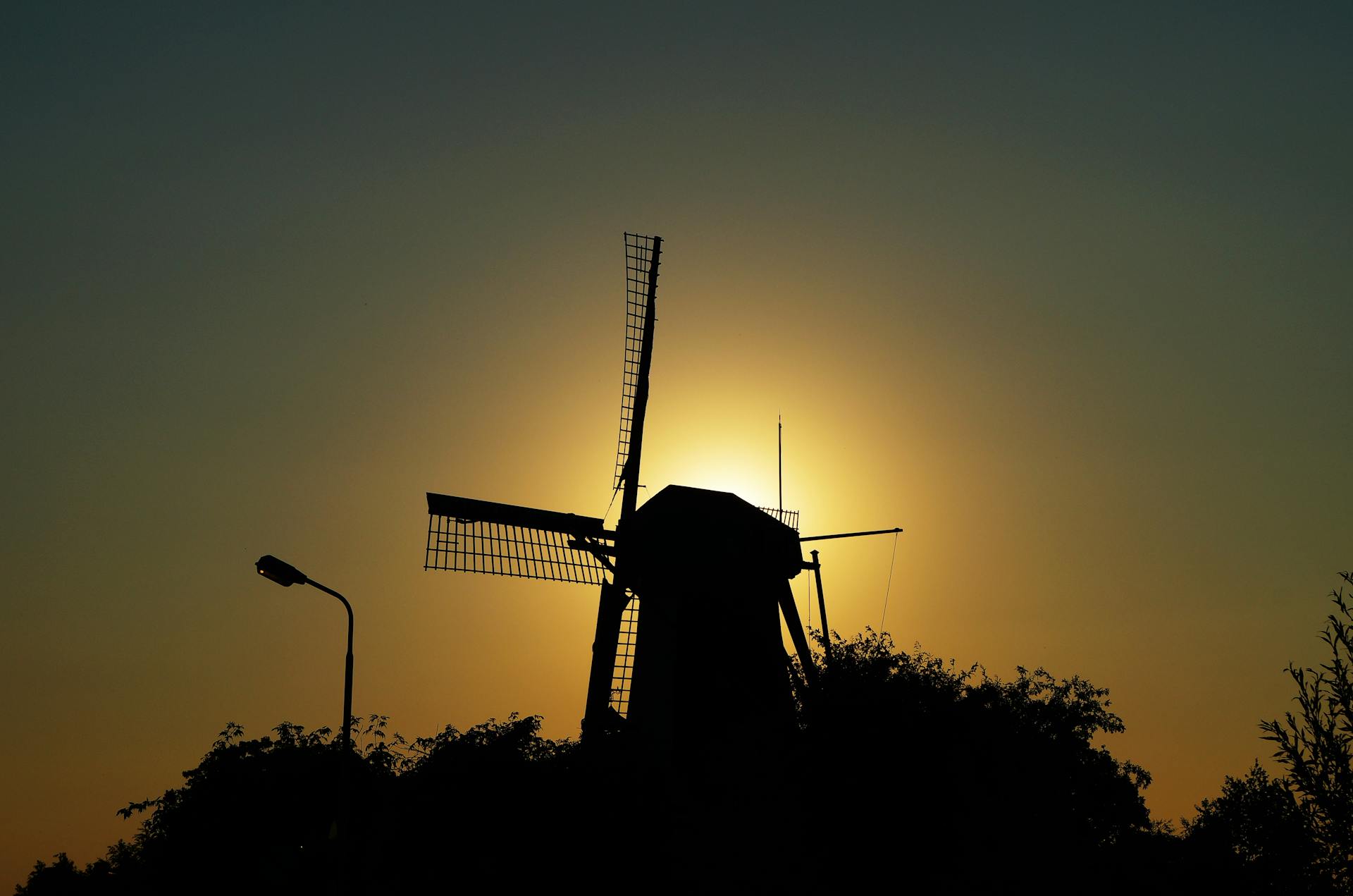 Silhouette of a windmill against a warm sunset sky, symbolizing renewable energy and tranquility.