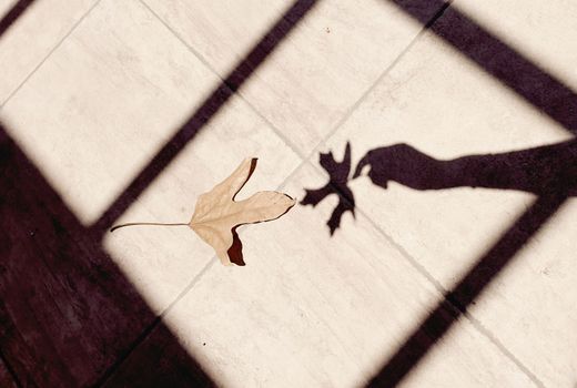 Creative shadow of a hand capturing a fall leaf on a tiled surface, evoking a sense of autumn.