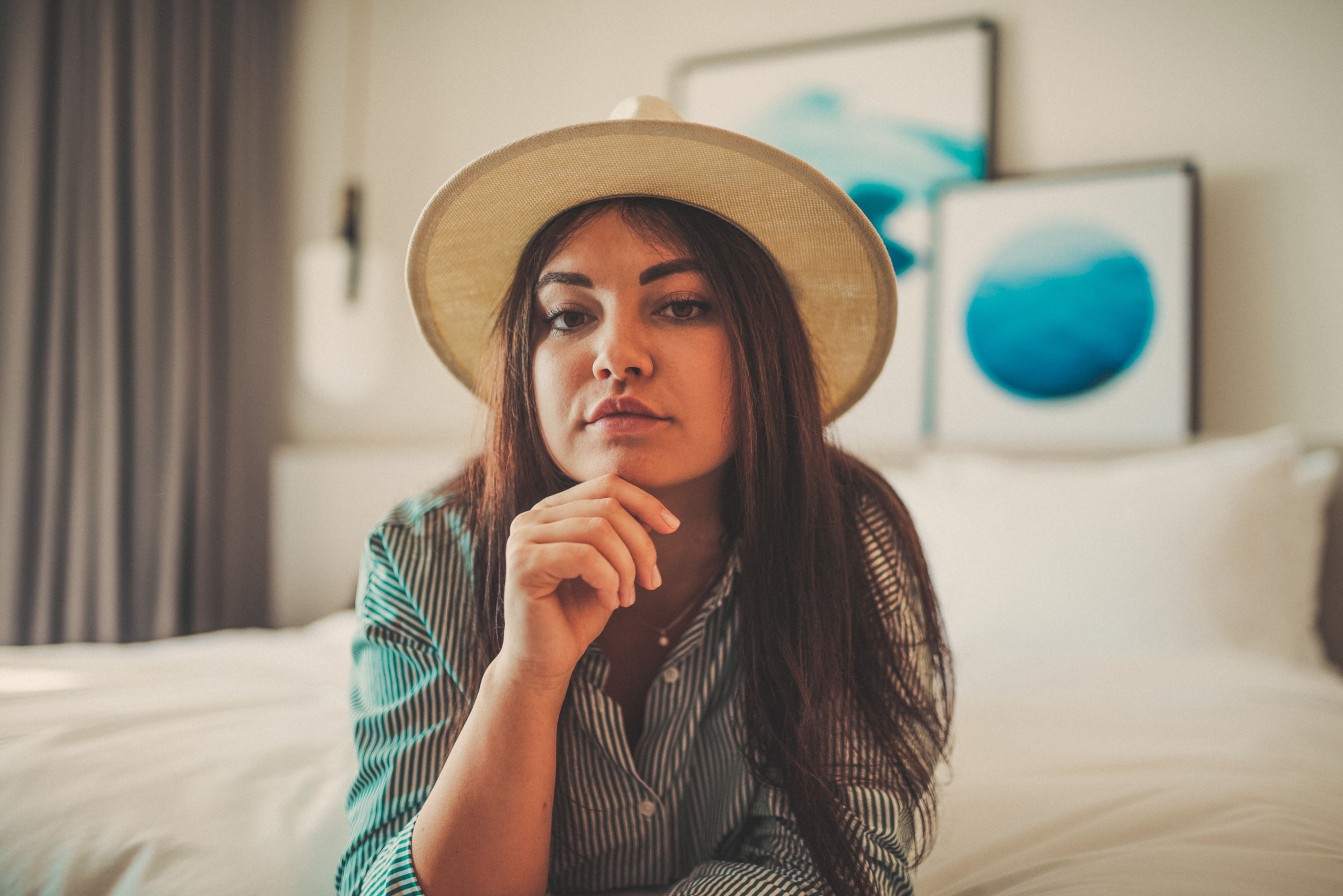 Woman with sun hat resting on bed in stylish indoor setting with modern art decor