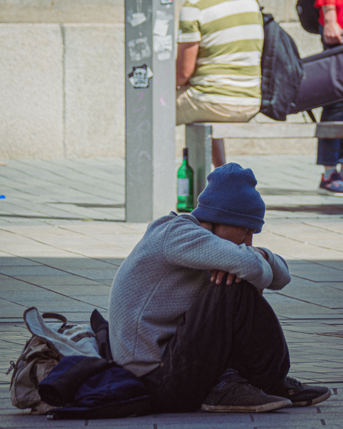 Free Person sitting on a sidewalk, head down, symbolizing solitude or contemplation. Stock Photo