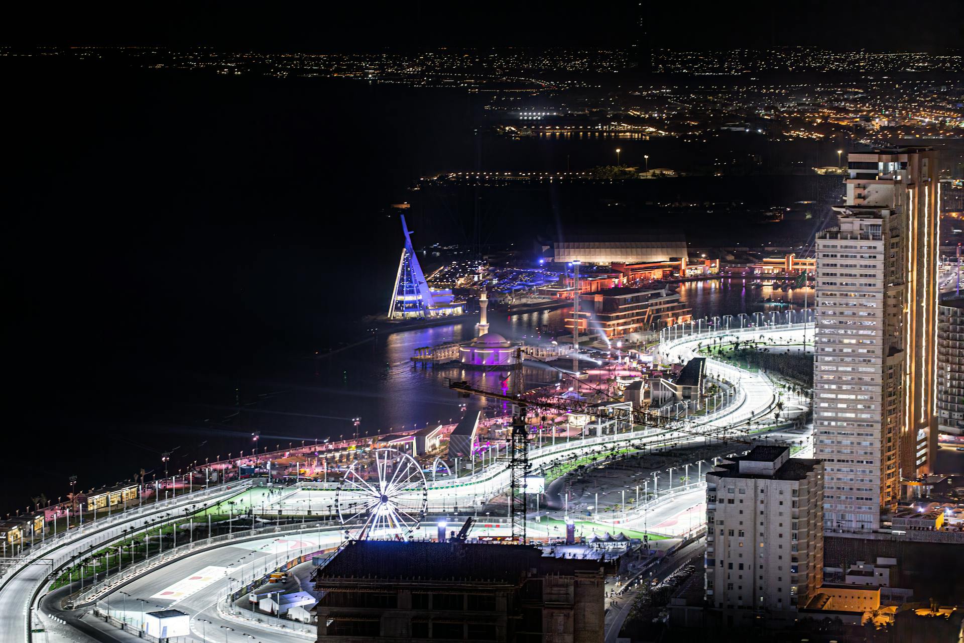 Vibrant night aerial view of Jeddah Corniche Circuit in Saudi Arabia with city lights and a Ferris wheel.