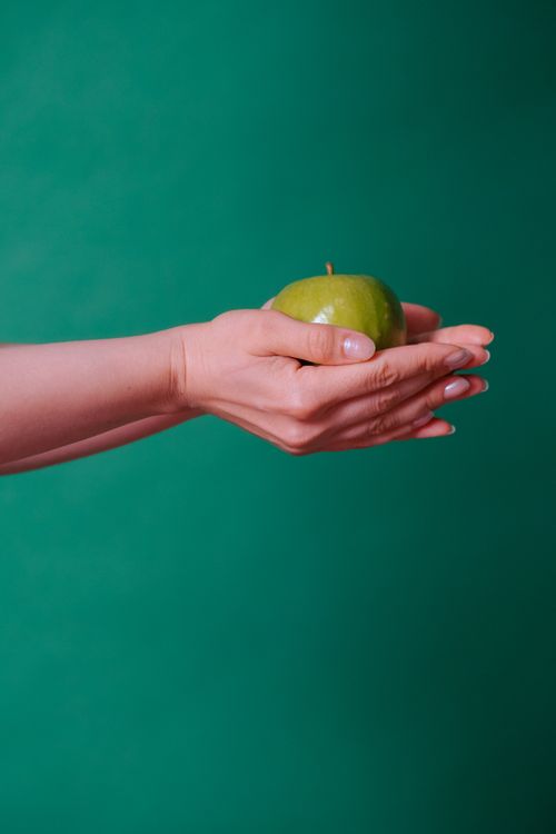 Free Close-up of hands holding a green apple against a green backdrop, symbolizing freshness. Stock Photo