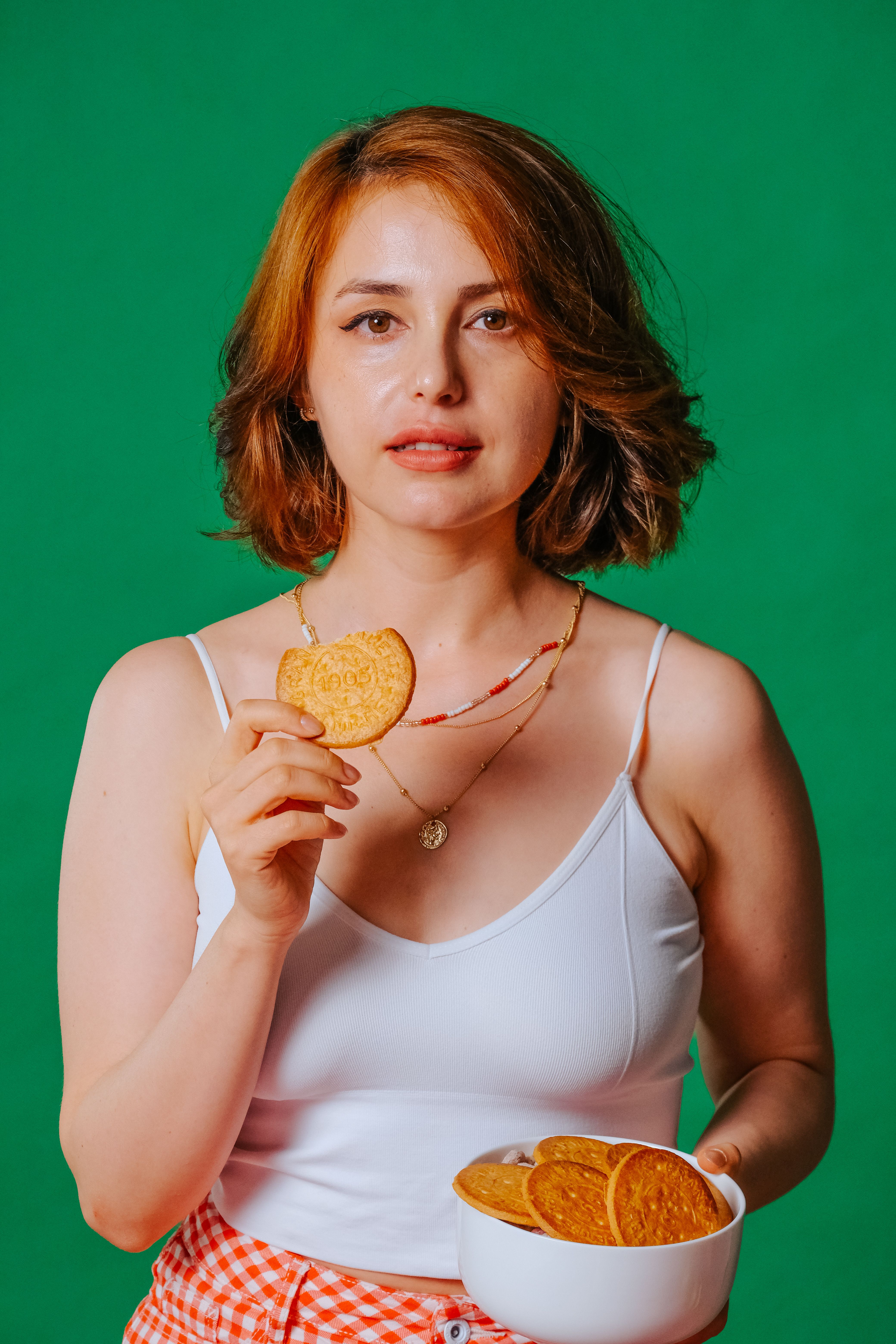 Confident woman in white top holding biscuits, set against a vibrant green backdrop.