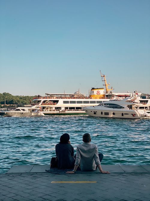 Free A couple sits by İstanbul's waterfront, enjoying the view of boats under a clear sky. Stock Photo