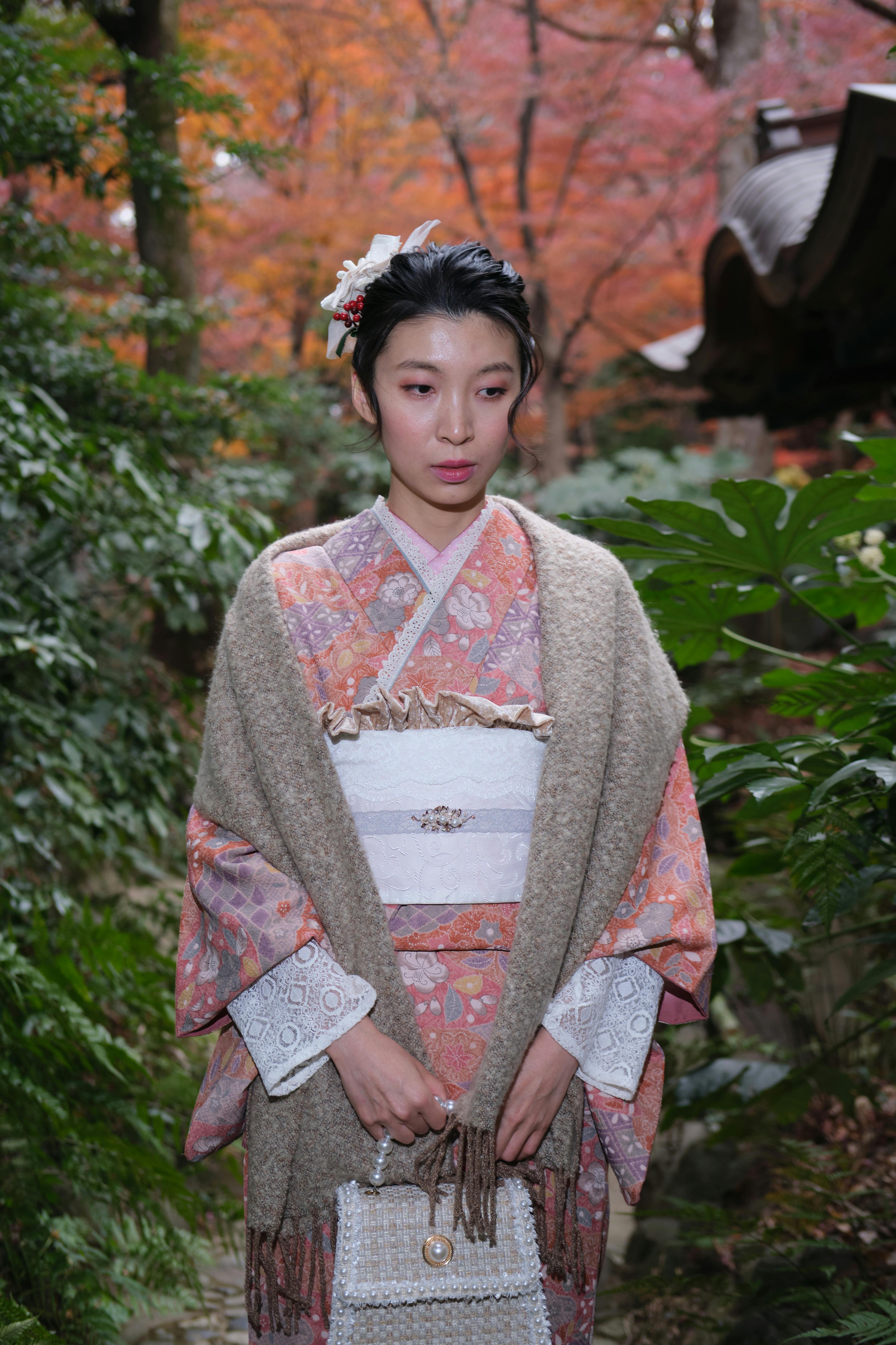 Asian woman in traditional kimono standing outdoors surrounded by autumn foliage.