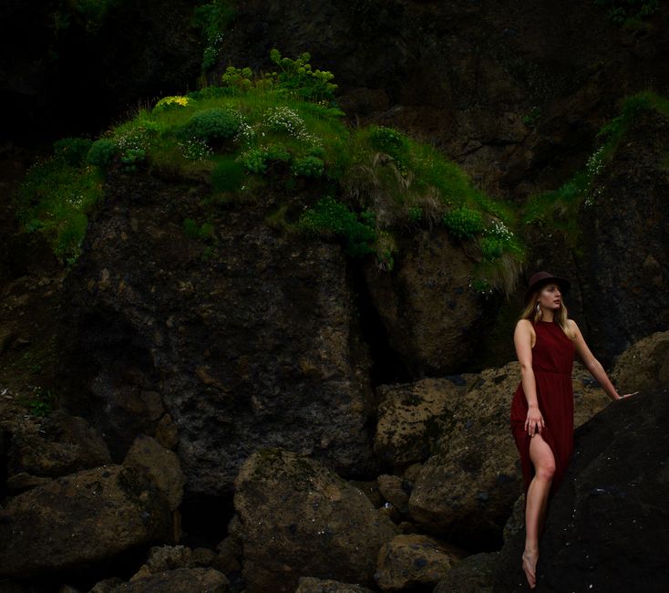 Artistic shot of a woman in a red dress standing on rocks in Vik, Iceland's natural landscape.