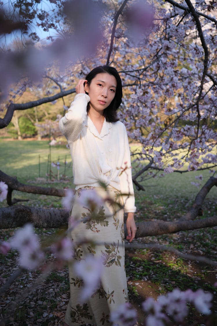 A Woman In White Long Sleeve Dress Is Standing Beside Tree